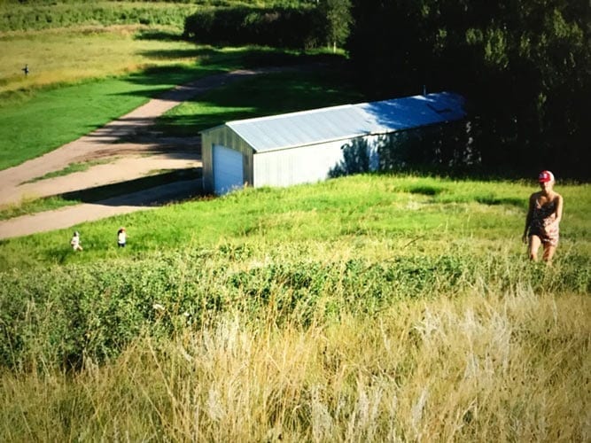 A family walks around a hilly field near a storage shed